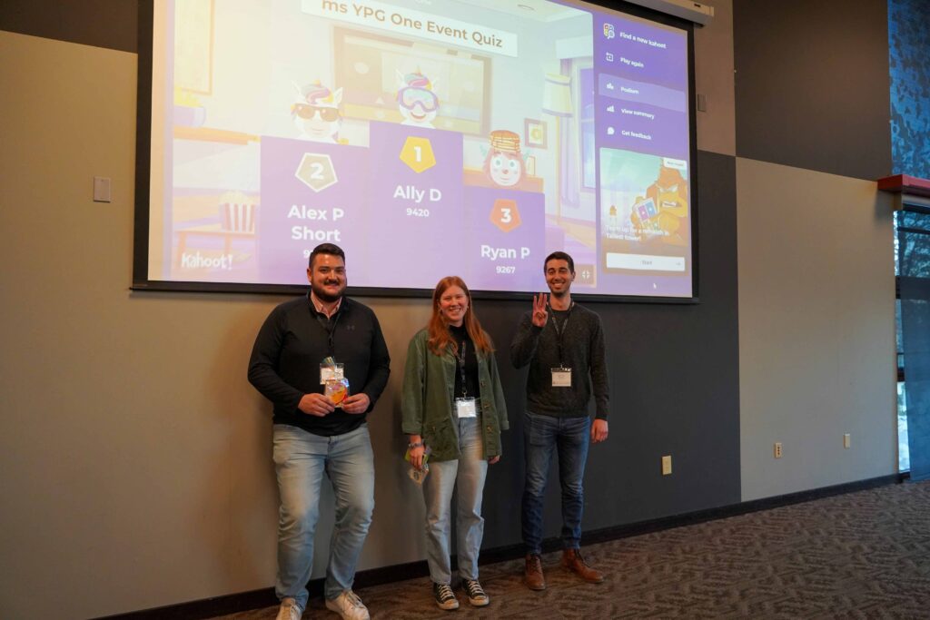 Three people standing in front of a presentation screen. They are celebrating winning a group game during a conference.